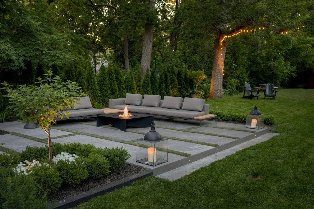 Lounging area surrounded by lush greenery with a fold fire pit in the middle
